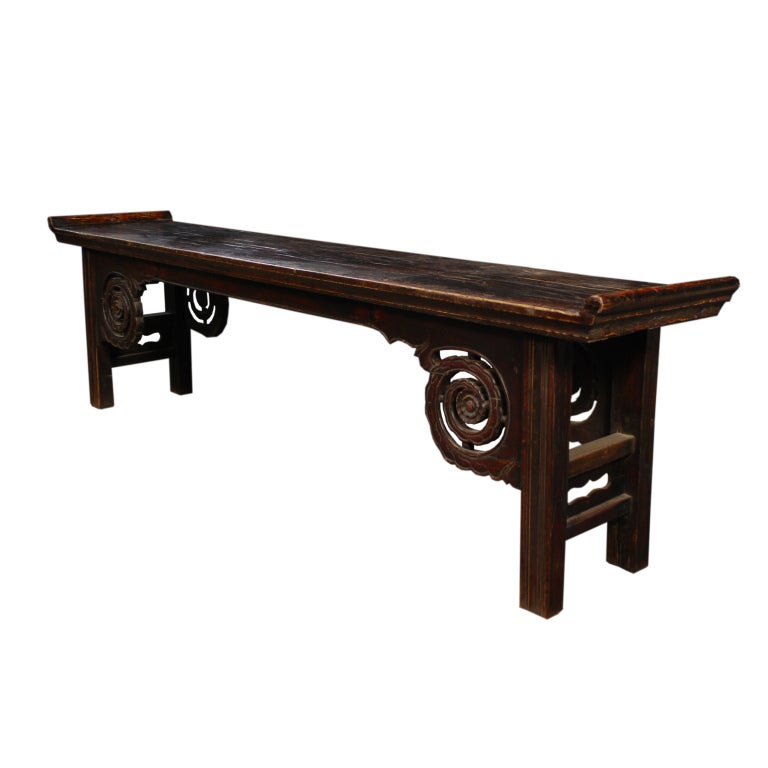 A 19th century Chinese elmwood bench with everted ends and carved phoenix tail and flower spandrels.
