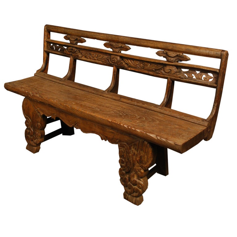 A 19th century provincial Chinese elmwood village bench with floral carved back, and heavily carved legs ending in scrolled feet.