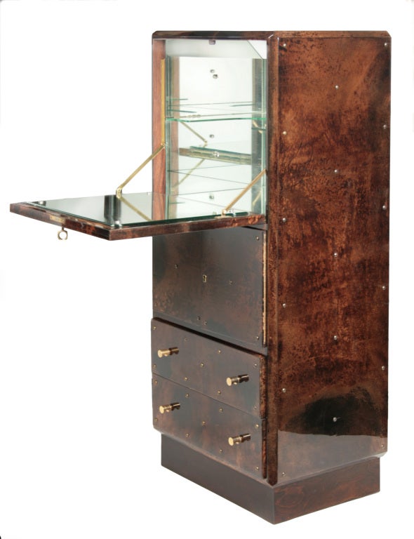 This is an elegant Aldo Tura bar cabinet covered in parchment. The upper interior cabinet is a mirrored bar, with one wraparound glass shelf. An interior light is actuated by a pressure switch to turn on when the front of the bar is opened. Below