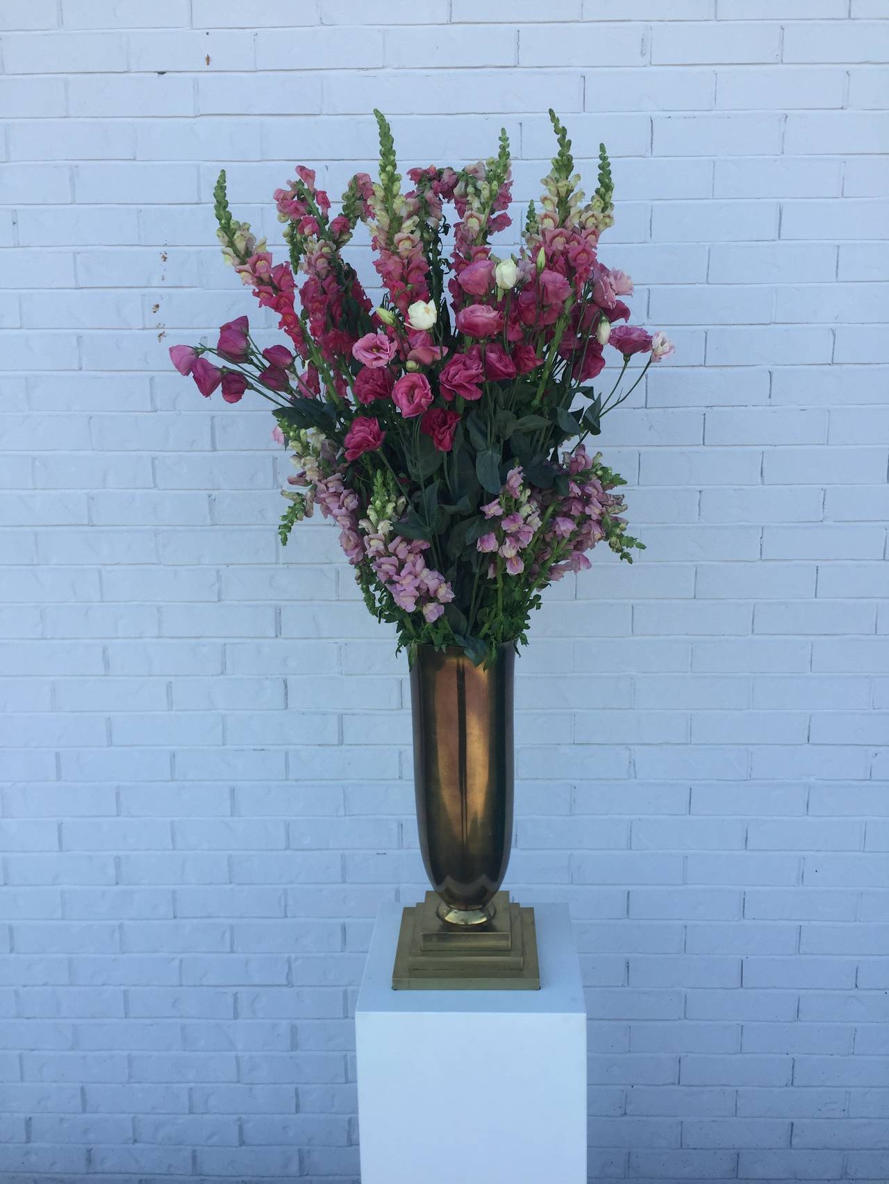 Pair of Art Deco period urns with stepped brass bases and elegant urn vessels with a bronze patina, minor dark spots on metal, dramatic as centerpieces, shown on white pedestal that is not included.