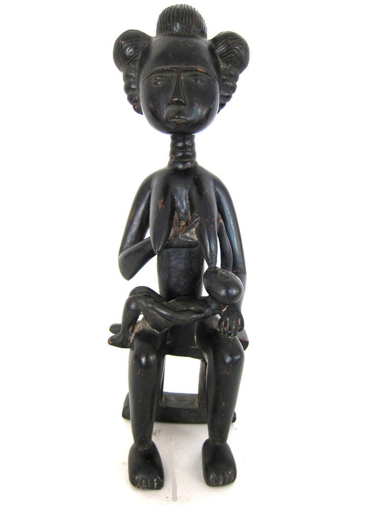 This wooden Statue of a Mother having 3 large rings on her neck and sitting on a Two Column Royal Stool breat feeding a child has fine body scarification designs Provenence available Well carved and beautiful patina Purchased by a collector in 1986.