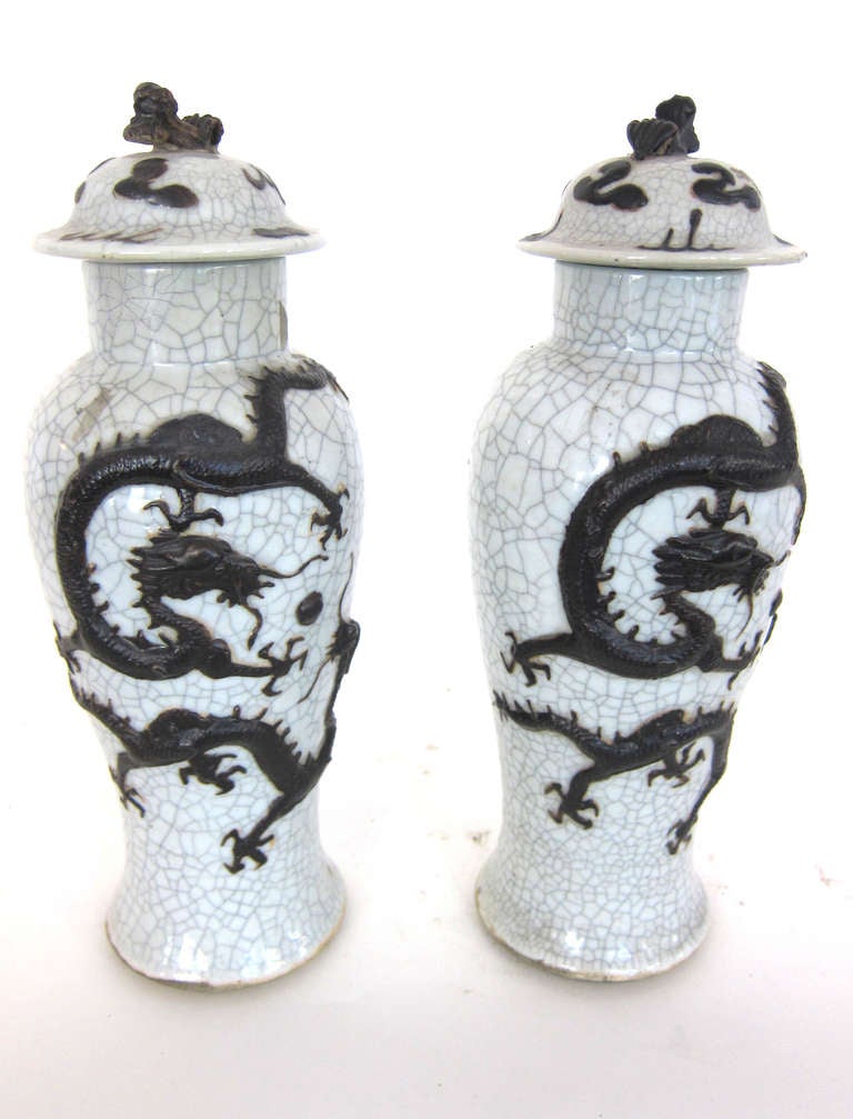 A pair of beautifully tapered 19th century Chinese Vases with Lids. These vases have a white crackled glaze with a matching relief of a dragon motif on the surface.