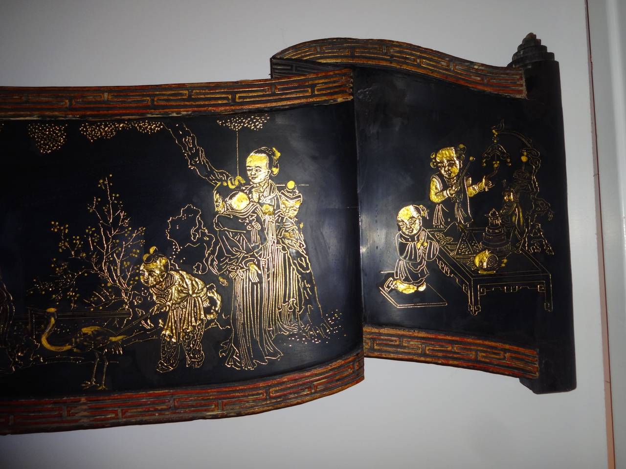 A Chinese hand carved black lacquer and gilt wood panel in a scrolling ribbon form decorated with hand carved groups of gilt figures, including a central figure atop a strutting rooster (for good luck.)