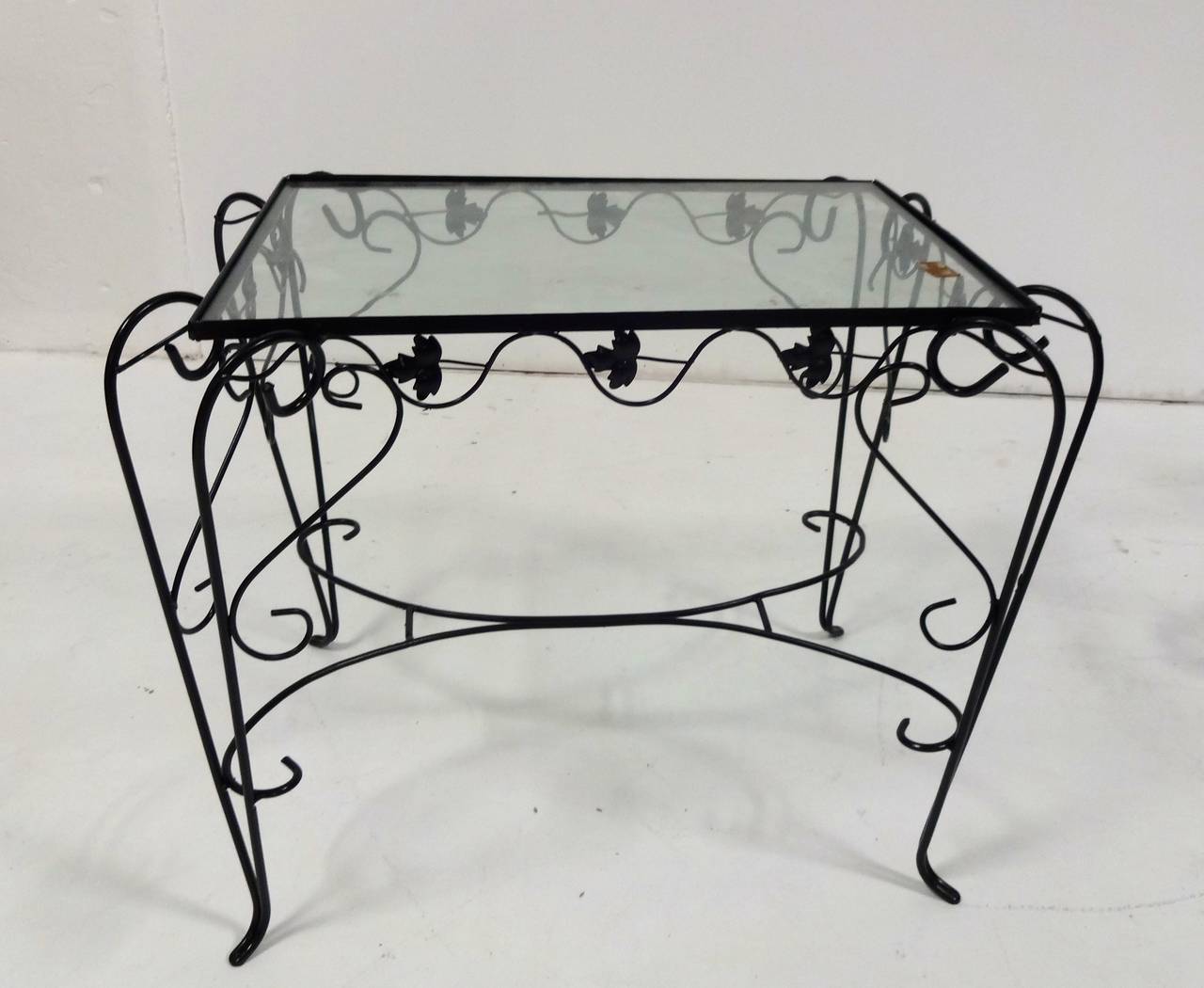 A wrought iron outdoor garden set comprising one rectangular table w/glass top (can accommodate a larger glass top) and four arm chairs with scrolling foliate motif painted black.  Cushions are not included. (Table measures 35
