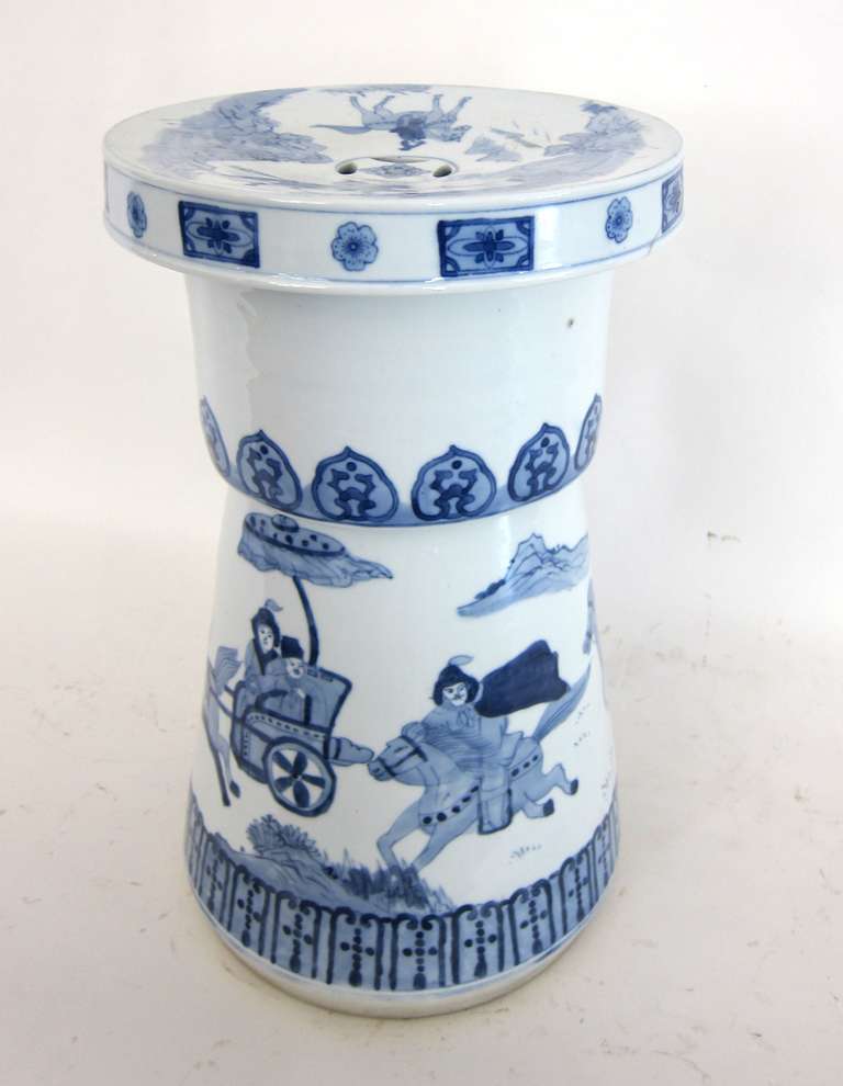 A hand-painted porcelain blue and white garden stool. A lovely painted scene of a rider on horseback and a horse drawn sedan chair. The seat has a painted scene with a pair of horse and riders.