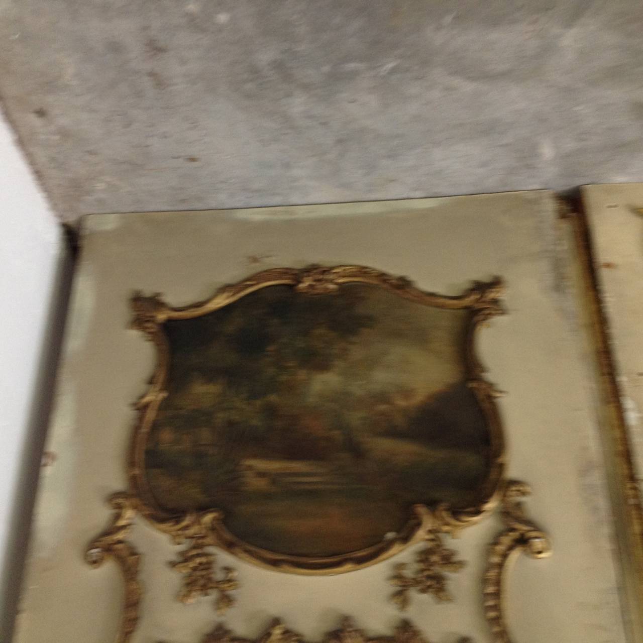 An eleven foot high French trumeau three piece wall mirror panel from the pied a terre of the Duke & Duchess of Windsor painted in Paris green with gilt accents. Oil on canvas three paintings of landscapes w/cherubs are inset above, with a pair of