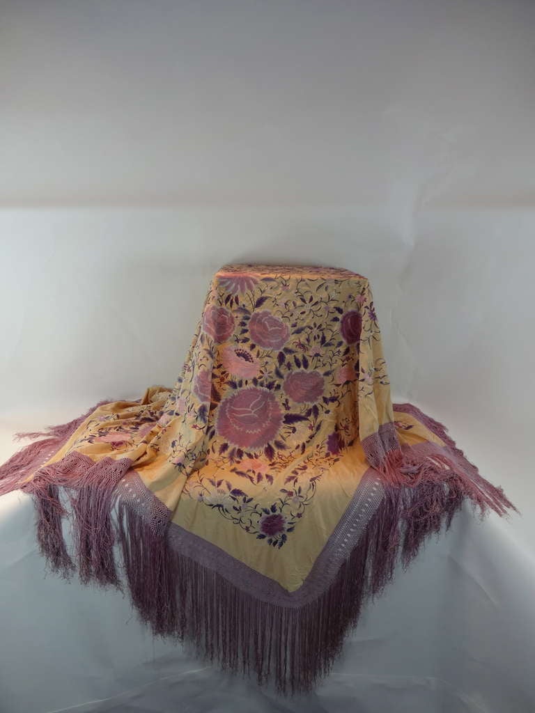 This hand embroidered hand made PIANO SHAWL has flowers over all in different colors of lilac to purple to lilac pink hand made fringe in lilac on a cream silk background. Mrs Ringling from the Circus family use to wear a shawl similar to this one