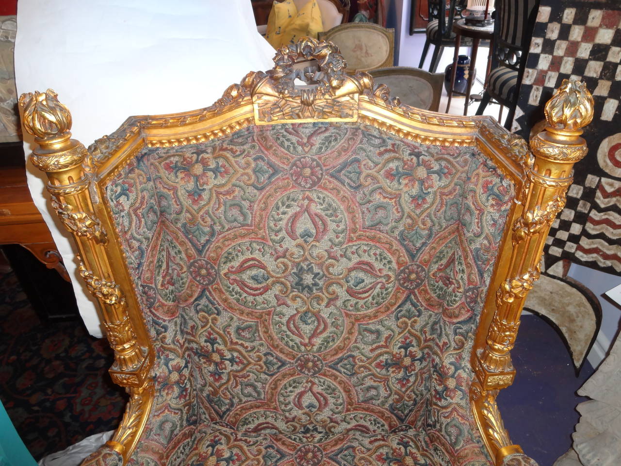 An ornately carved giltwood bergere à oreilles (closed arm chair), back centered with laurel wreath, sides have beautifully carved torcheres with entwined garlands terminating in flames. The fluted front and side apron have draped flower garlands