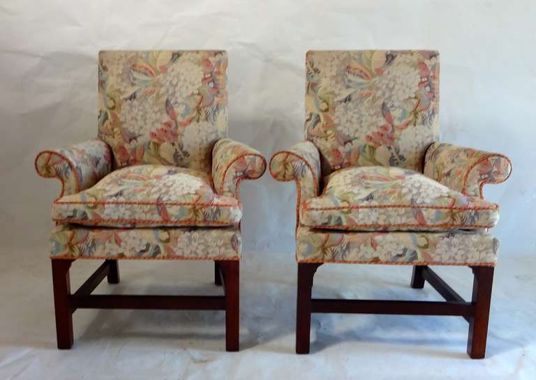 A pair of traditional club chairs with tight back, loose down cushions, upholstered in woven tapestry fabric trimmed in a rust colored twisted cord welt, with dark wood straight legs and stretcher, from Baker Furniture.
