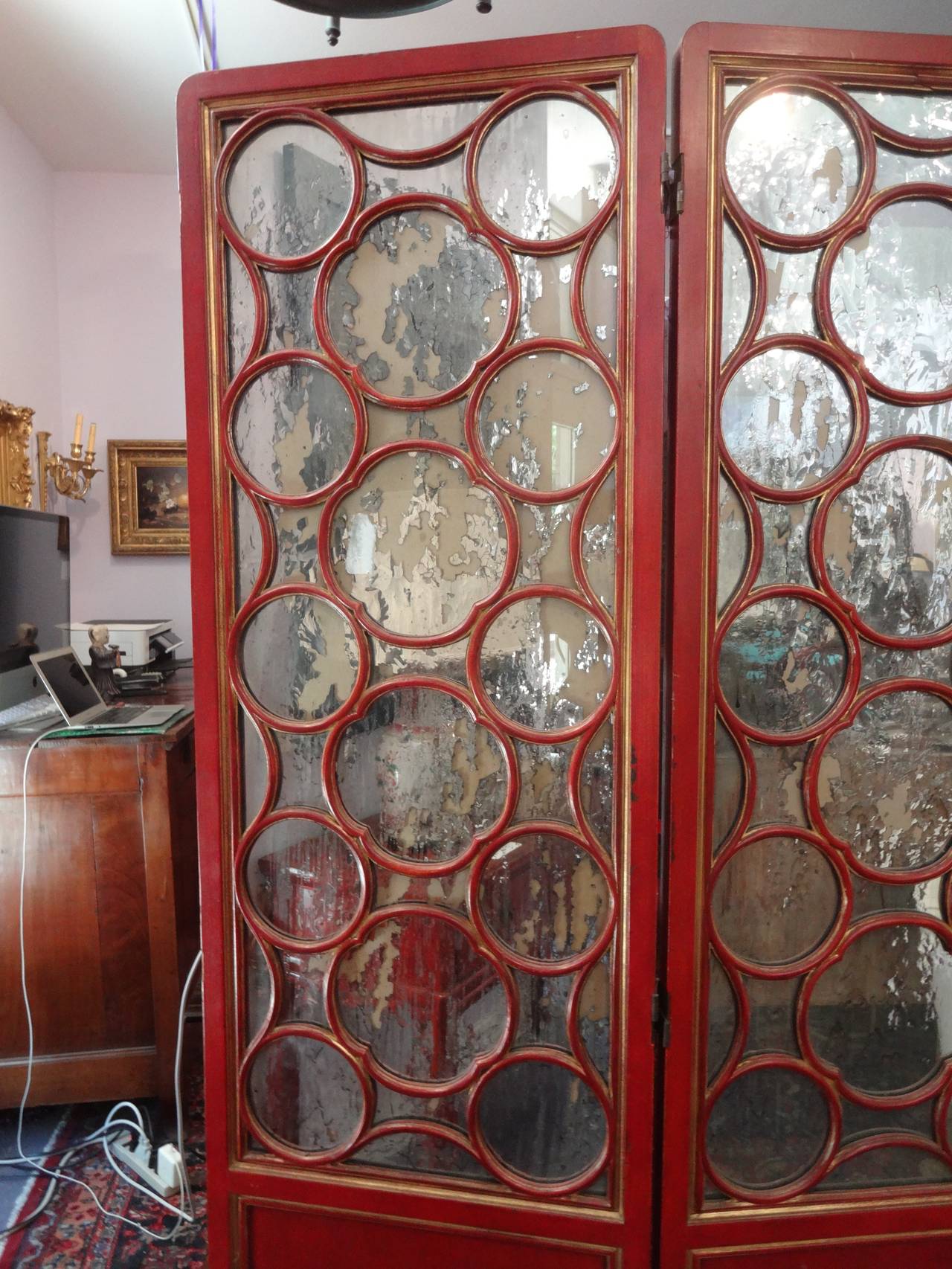 A Glamorous James Mont Chinese-modern style three panel mirrored folding screen (folds both ways) painted red with gold accents. Top panels have a circular motif over distressed silvered mirror. Each panel is 18.5 wide.