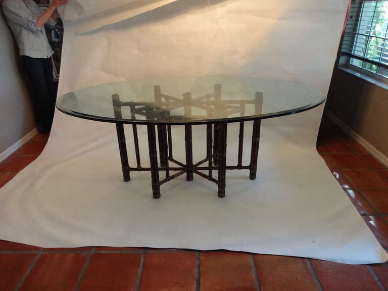 This McGuire Dining Table has an 
Oval glass top has a beveled edge sitting atop a natural dark stained 