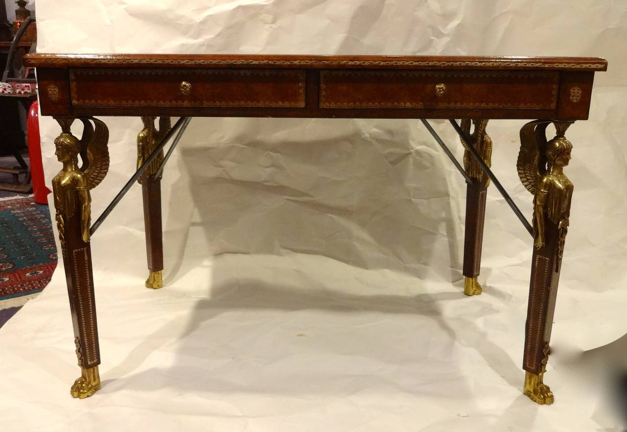 A French Empire style desk with 2 drawers upholstered in gold tooled leather, ormolu mounted winged goddess caryatids on four legs, ormolu paw feet by Maitland Smith.  Original label in drawer.