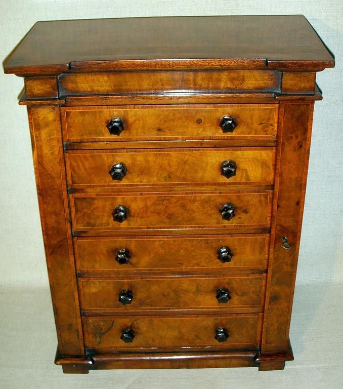 Miniature Burl Walnut Wellington Chest/Specimen Cabinet with Six Drawers Fitted With Interior Glass Inserts.  Drawers are Ornamented with Satinwood Crossbanding and Amber Glass Knobs.  Right Side of Frame Overlaps the Drawers, is Hinged, and Fitted