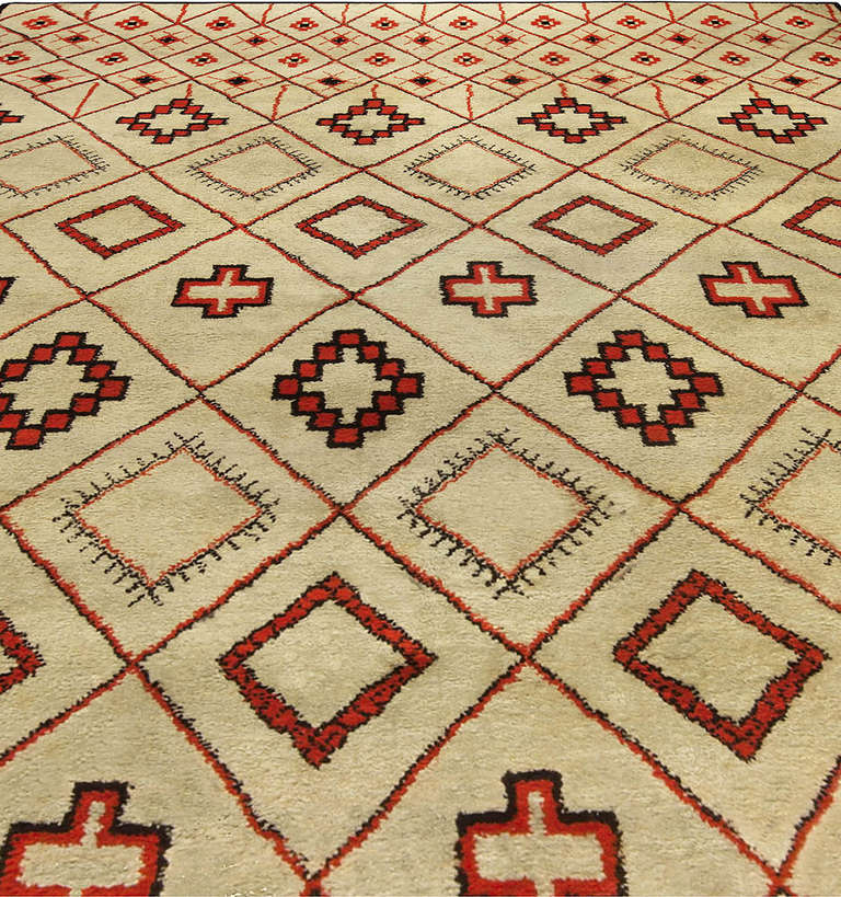 A Vintage Moroccan Rug woven in the 1930's with a play on the traditional diamond shapes and also cruciforms. The design is geometric and less simplistic than the designs seen in Moroccan rugs woven after 1940. Red, black and Ivory with a gradation