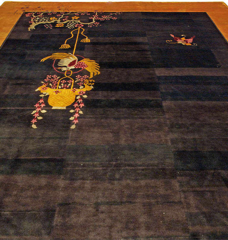 This Art Deco rug from China has an open striated dark field with naturalistic floral motifs sparsely placed in the composition within a open gold border. This is a classic example of Chinese Art Deco rugs produced in the early mid 20th century.