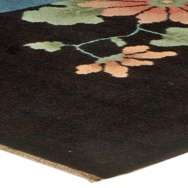 An Art Deco Chinese rug with a bold design of stylized landscape and realistically depicted blooms, in vivid colors, on a contrasting black background.