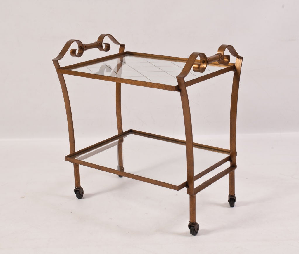 French metal bar cart with a gold finish, glass shelves, and wheels.  Top glass shelf has a gold diamond pattern; bottom glass shelf is plain.