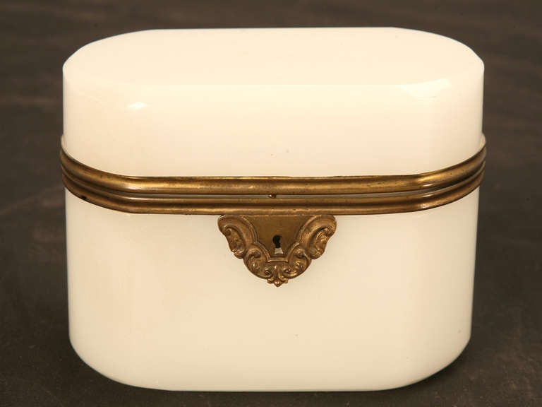 Antique opaline glass box with brass trim. All corners are rounded and the top is hinged. Shows wear on bottom and top, as well as a small chip on top radius.
Opaline boxes were used to hold tea and sugar based candies. They were held only for the