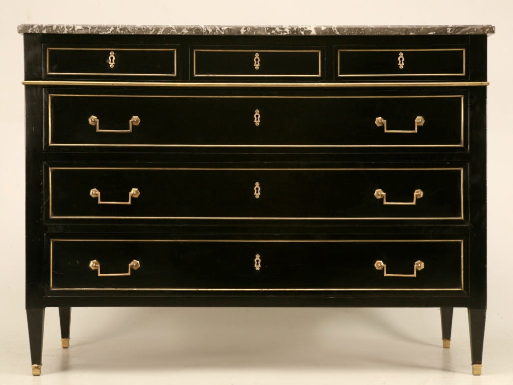 Absolutely breathtaking antique French Louis XVI style 3 over 3 commode retaining it's original dark marble top. The black ebonized mahogany finish is deep and rich, providing an elegant contrast to it's polished original brass trim. Storage abounds