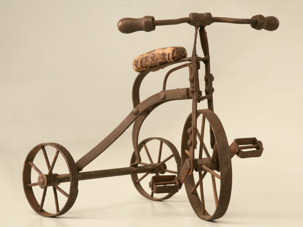 Unfortunately we don't know much about this handsome steel tricycle, though what we do know is that it is very charming. Well constructed miniature steel tricycle with it's aged leather seat would be the perfect accent in a gentlemans office or