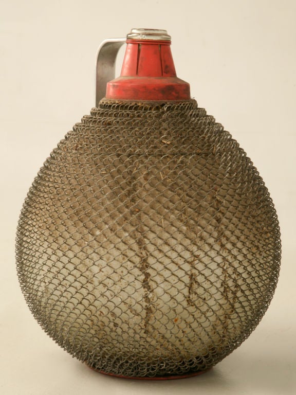 Wonderful industrial themed wine jug encased in wire mesh with a sturdy metal handle. Whether you decide to use this as decoration or not, this is so great looking it would even make a great lamp.