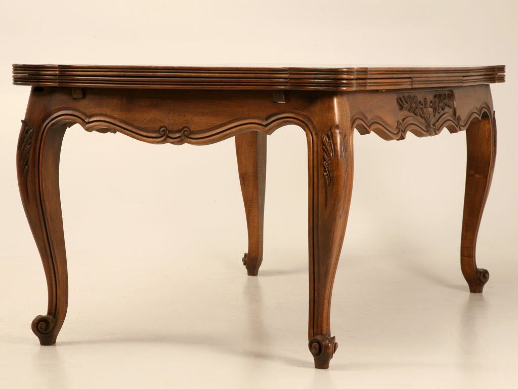 Exquisite beautifully carved vintage French walnut draw-leaf dining table depicting a majestic winged urn motif on the scalloped aprons. This table is stunning from its outstanding medium color-tone showcasing the exotic grain of the walnut down to