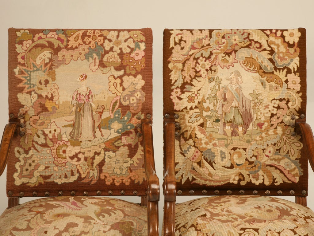 Striking pair of antique French walnut Louis XIII throne chairs with exquisite needlepoint upholstery. Ready for hosting dinner parties from either end of the banquet sized table, receiving guests and visitors to your stately office, or flanking the