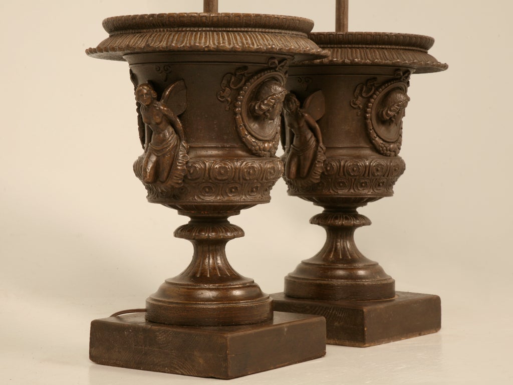 Remarkable pair of Italian Iron Urns with intricate details cleverly fitted as a stunning pair of Table Lamps. Perfect in scale for large rooms, this pair have winged maidens, and portrait medallions as decoration. Used indoors or out, these fine