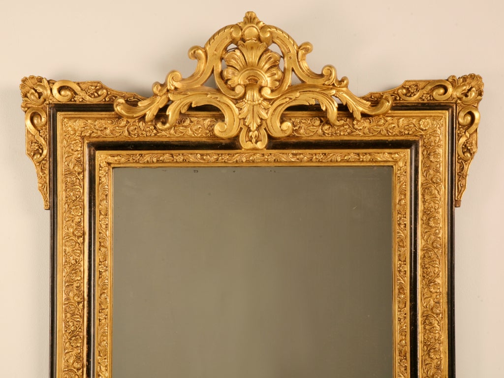 Stunning ornate original antique French mirror with a glamorous gilded and ebony accented frame. This fine mirror is the bees knees, it is striking without being pretentious. Perfect utilized in any room of the home, this glamorous mirror will fill