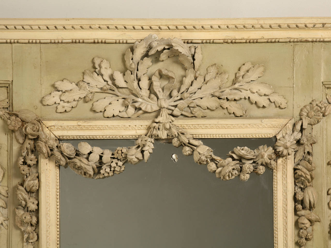 Antique French mirror probably made in the mid-1800s with an ornate and intricate hand-carved relief consisting of urns, floras and leaves. Built-in to an early Parisian apartment. It's muted celadon green and cream colors are calm and soothing,