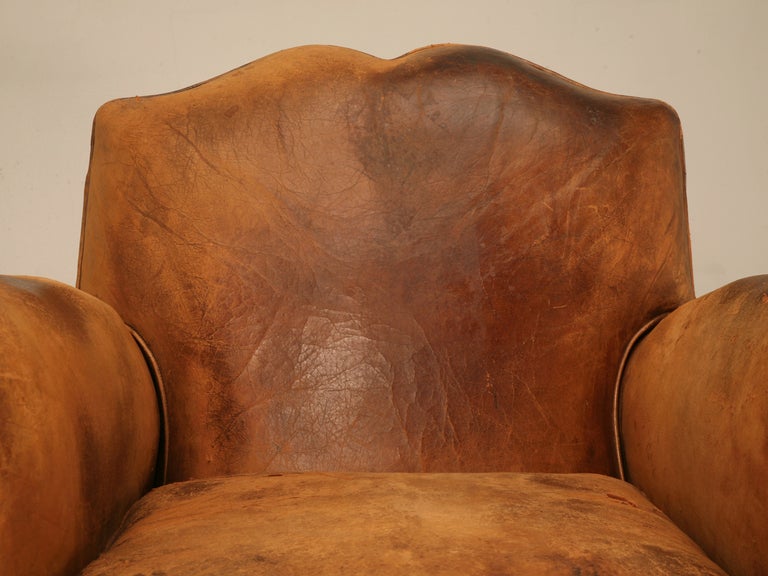 Incredible pair of original vintage French leather club chairs retaining their striking and spectacular original leather. Spot on with tons of character and charm, this pair offer the highly coveted moustache backs and have a unique design
