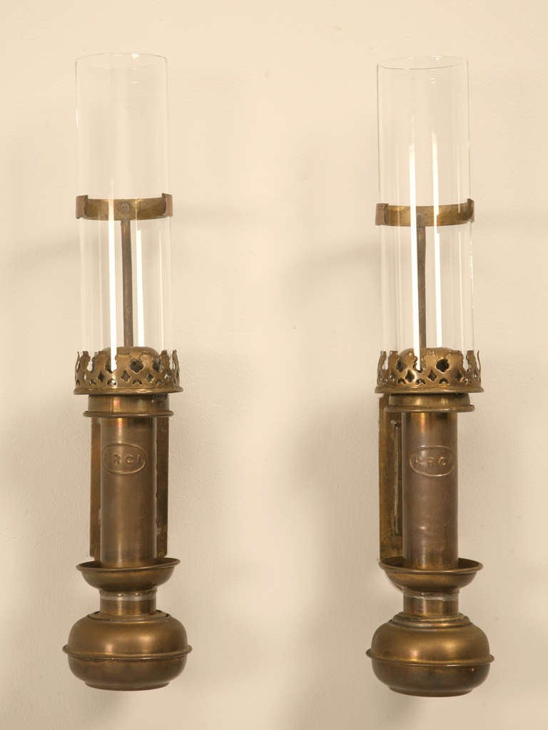 Pair of early original antique French brass and glass railroad sconces. Utilized in passageways and common areas before the invention of electricity. Retaining their original wavy glass cylinder shaped chimneys, it appears as though these were kept