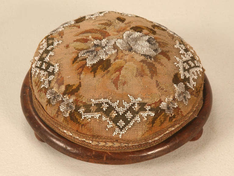 Elegant and sophisticated antique English ladies tuffet or footstool with a charming hand beaded cover. Intricately detailed with a large center rosette, the edges are bordered with an interwoven vine of greenery dotted with more flowers. Retaining