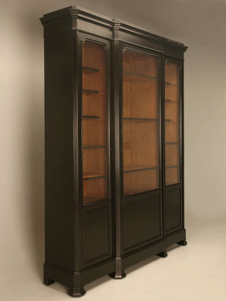 Recently received as part of a 3 piece library set with a desk and chair, this 3 door bookcase offers adjustable shelves, while retaining important original features such as its wavy glass doors and an un-touched ebonized finish.  A standout, this