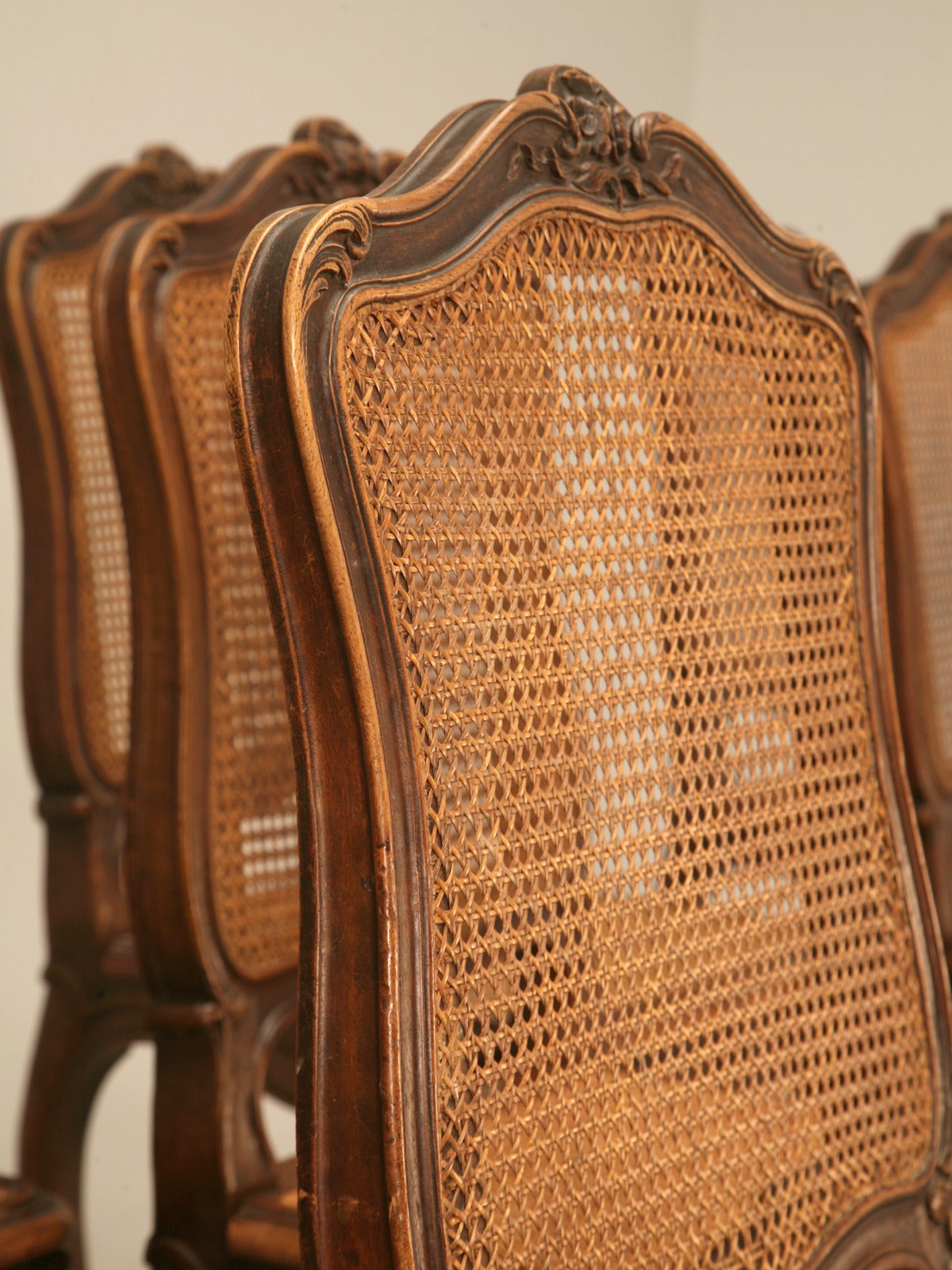 Circa 1880-1900 Set of twelve Louis XV style French walnut dining chairs in as found condition. We were all set to have the two chairs re-caned, and then someone asked us about upholstering the chairs and removing the cane. We would be happy to run