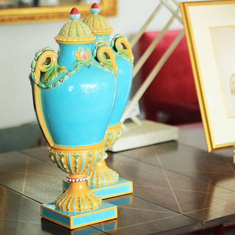 A pair of English majolica urn-formed covered vases. The palate is a strong turquoise blue with mustard yellow trim and rose colored details. Impressed under one base: 