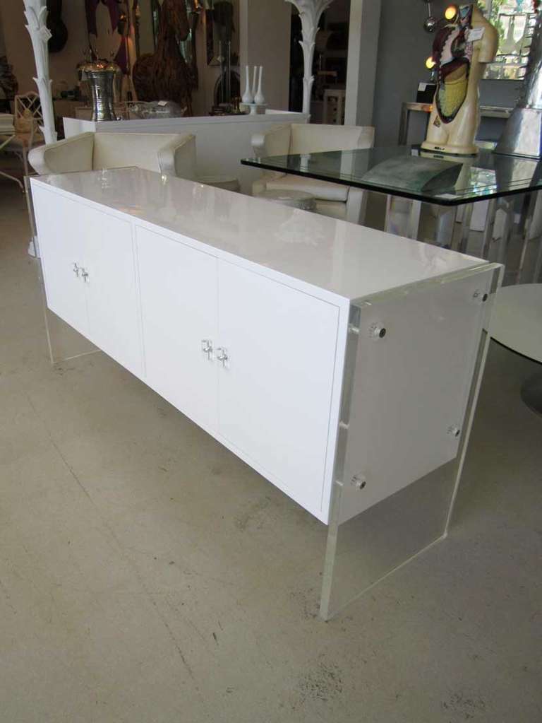 White lacquer credenza featuring lucite side panels and knobs on each of the four doors. This vintage cabinet is designed in the style of Milo Baughman .