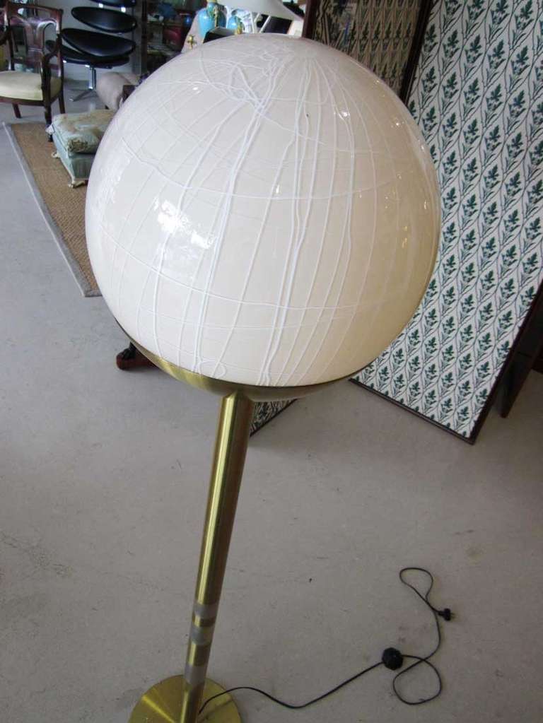 Tall vintage mod  floor lamp featuring a Murano glass ball that has 'drizzled' white lines pattern. The glass dome is supported by a two tone brass and stainless steel rod.  The fixture has a step switch for easy on and off.