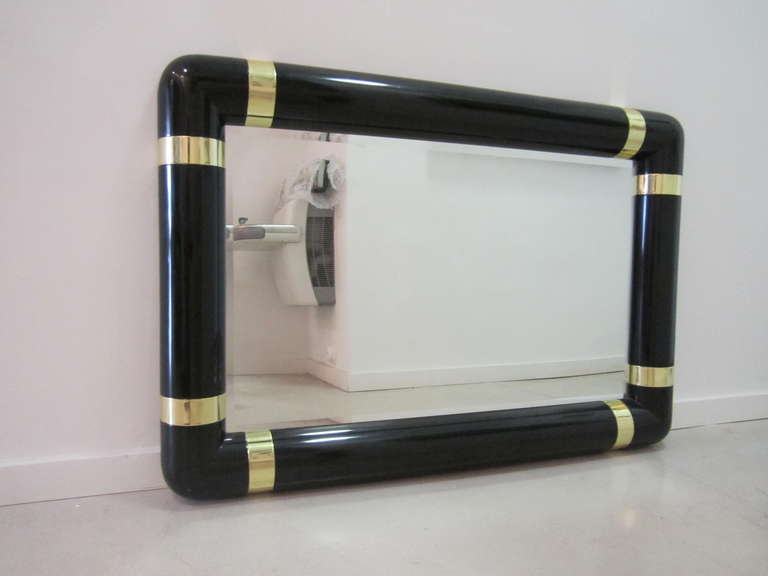 Minimalist black lacquered mirror with contrasting brass straps on each corner.