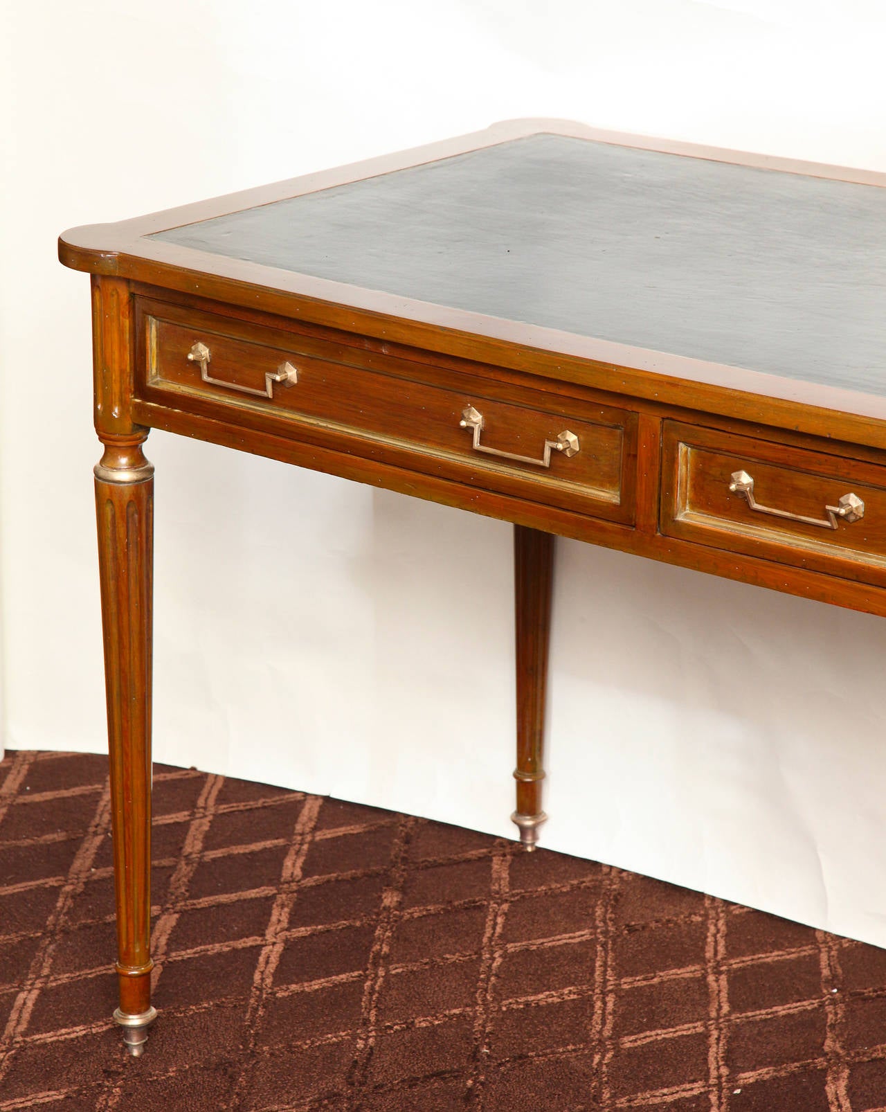 A French Louis XVI style fruitwood writing table finished on four sides and having two drawers in the apron with brass pulls. The top with rounded corners and inset black leather surface supported by four round tapering fluted legs with brass sabots.