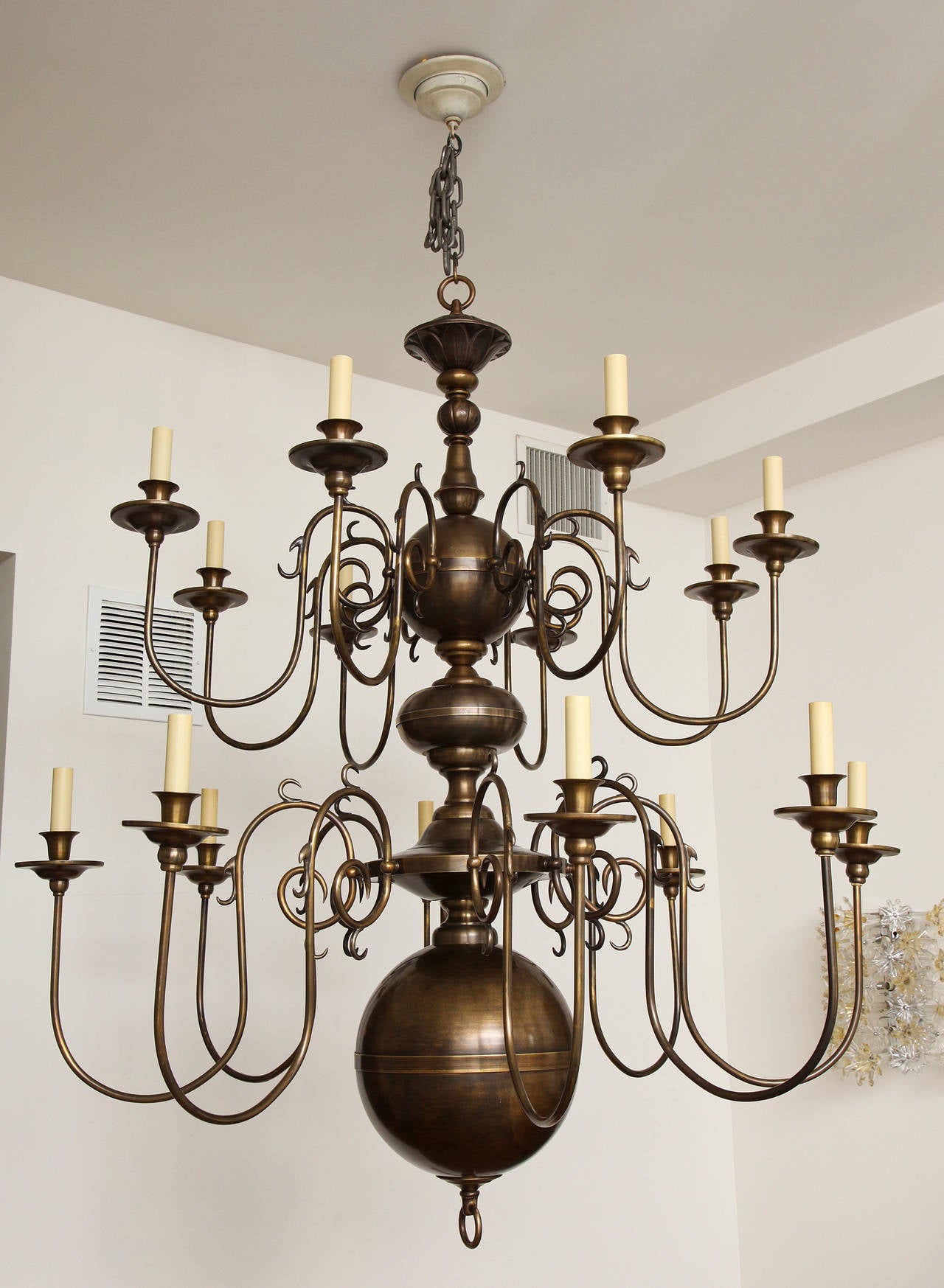 A two-tier sixteen-light Dutch style chandelier with rubbed bronze finish and oversized ball at underside with raised horizontal line at centre. The centre shaft with round and bun shaped elements.
Fixture fitted with sixteen candelabra sockets.