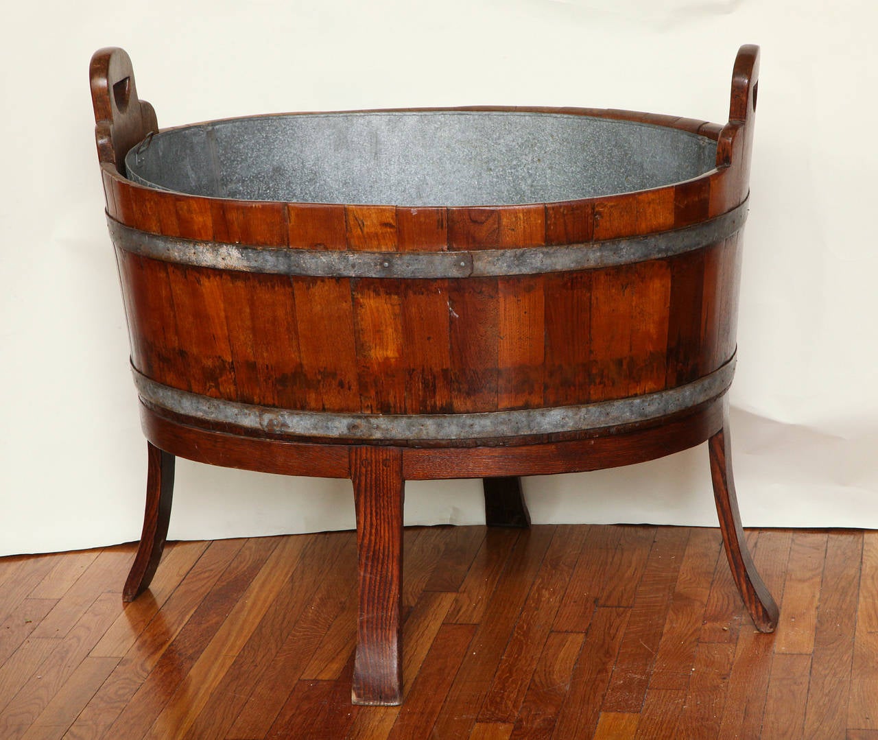 An English oval wine cooler, the oversized barrel constructed wooden body with cut-out handles and zinc liner supported by four splayed legs. Provenance: A Parish Hadley interior designed for Mrs. Charles Englehard.