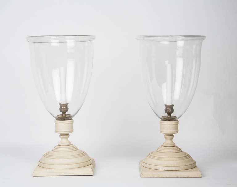A pair of English Georgian-style hurricane lamps, the turned bases with square plinth and oversized bobeche securing glass hurricane shade with molded edge and bronze candle fitting.