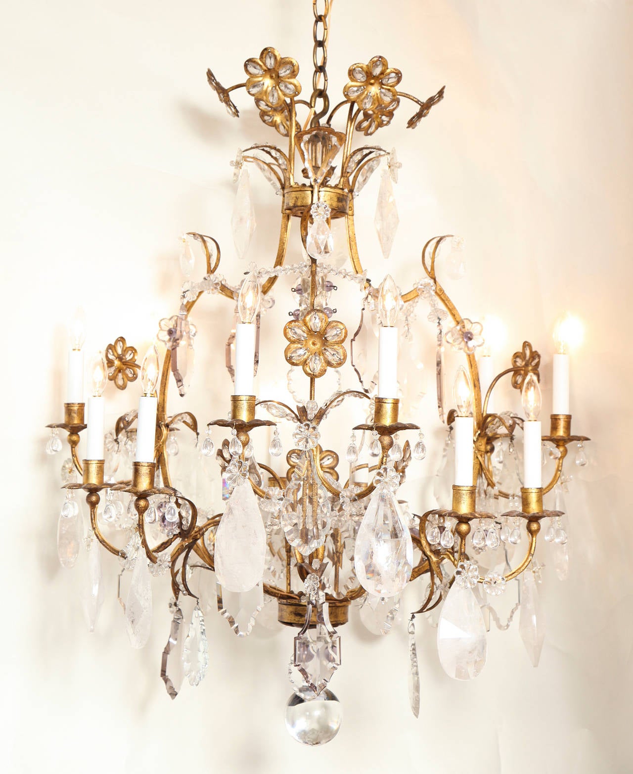 A twelve-light gilt iron cage form Louis XV style Baguès chandelier, the arms of staggered height issuing from frame draped with rock crystal and faceted crystal drops. The center with stems of flowers with inset crystal beaded petals. The frame