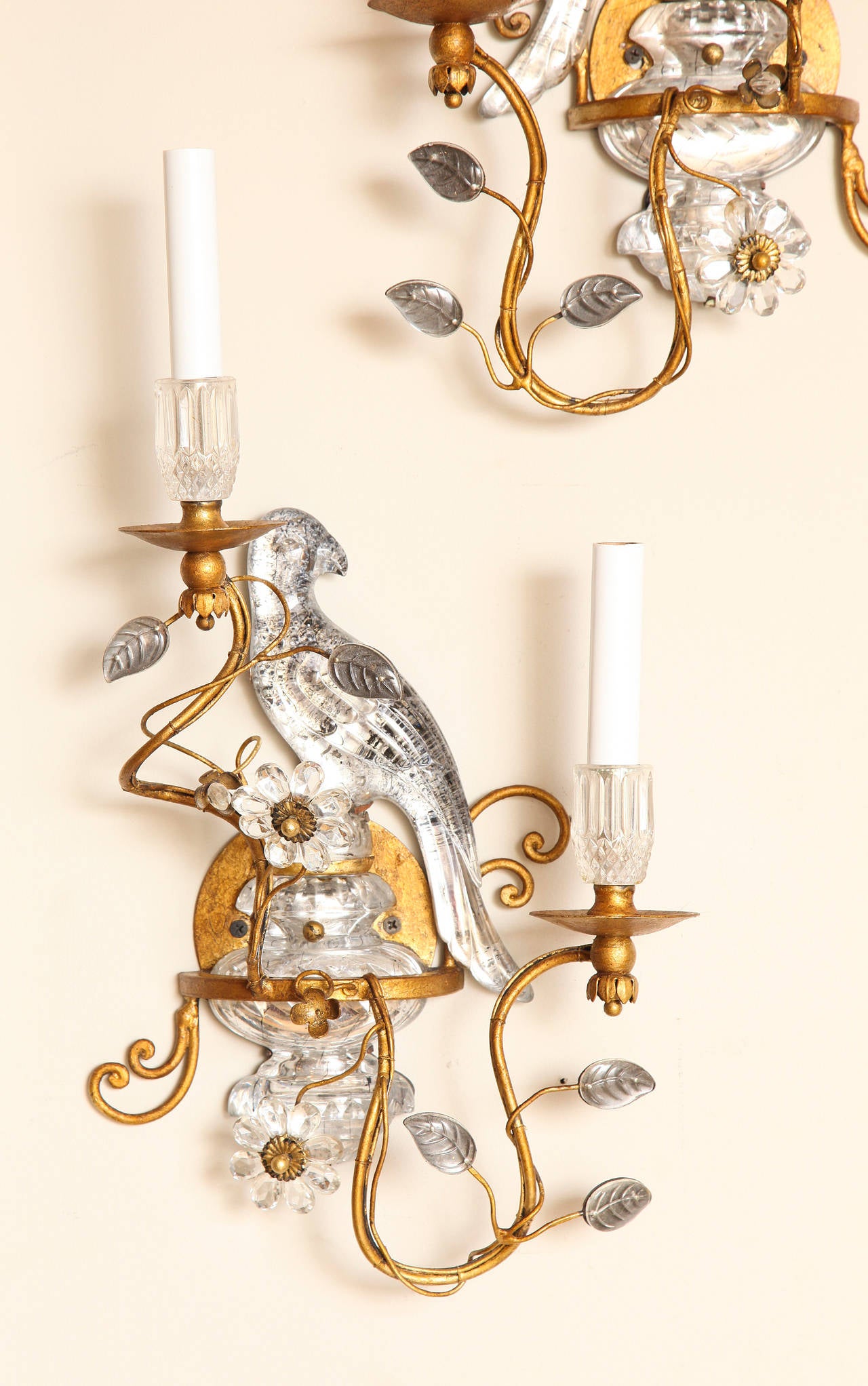 A pair of two-light Bagues style crystal and bronze bird sconces. The crystal urn-shaped backplate issuing metal branches and sprays of crystal leaves.