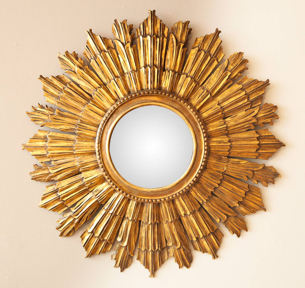 An Italian carved and gilt wood sunburst mirror. The round mirrored center framed with bead work issuing tapering wooden rays with irregular pointed ends. The center with convex mirror glass.  

Diameter of mirror: 7.5