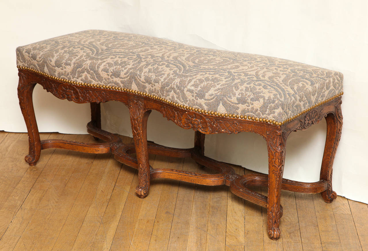A French Regence style carved fruitwood bench with serpentine apron supported by six cabriole legs and apron with shell motif. The legs joined by c-shaped stretchers with center rosettes. The newly upholstered seat covered in an Elizabeth Eakins