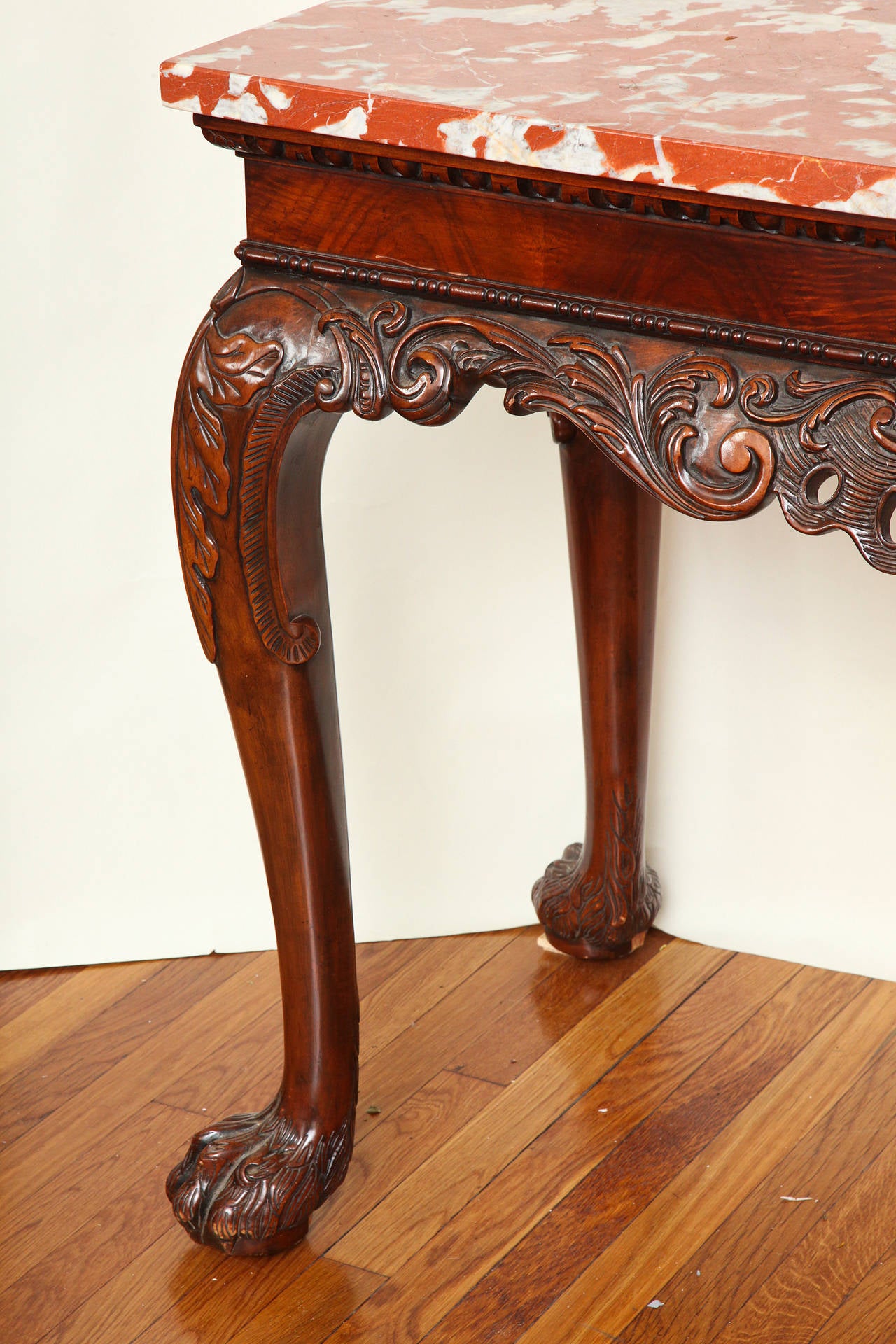 A Pair of English George II style hand carved mahogany side tables with shaped apron having open fret detailed acanthus leaves and scrolls. The crotch mahogany veneered apron with beadwork molded edge and egg and dart motif below marble top. The