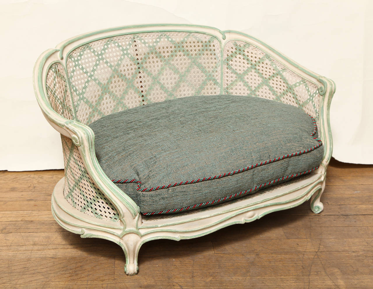 A French Louis XV style white painted caned dog bed. The arms with leafed shaped detail, the arched back, sides, and base with contrasting green striping. The back and sides with trellis patterned stenciling. The frame supported short cabriole legs