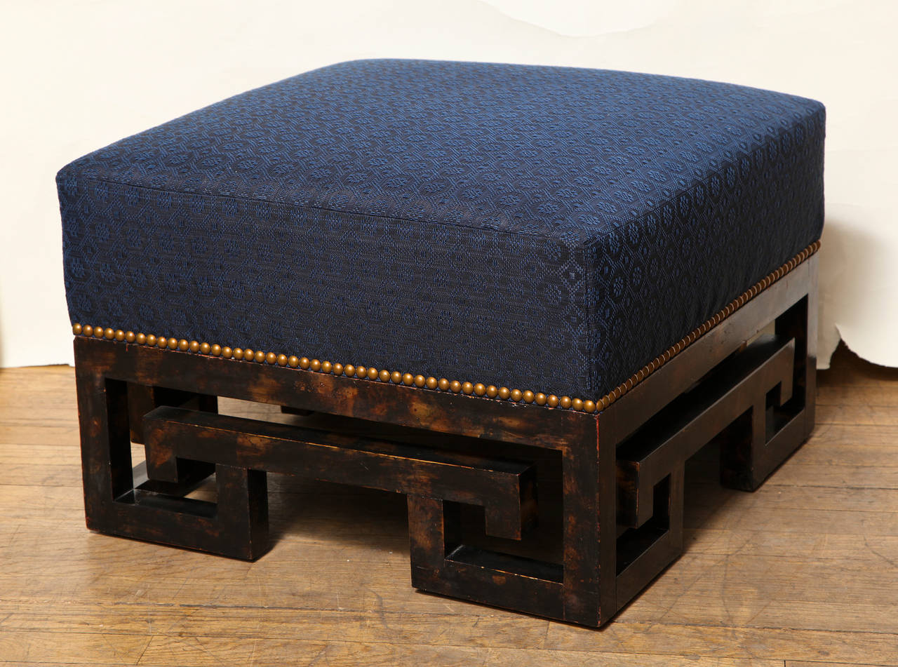 A square American low ottoman with wooden base in the form of open Greek fret motifs, painted faux tortoiseshell. The square upholstered upper section covered in blue horse hair with nailhead trim.